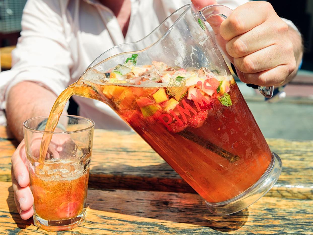 A man pouring a mixed Pimm's cocktail drink containing Pimm's, Lemonade, fresh fruit, mint and ice from a branded jug into a glass.