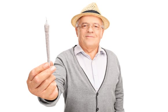 A senior man holding a rolled cannabis joint in his outstretched right hand.