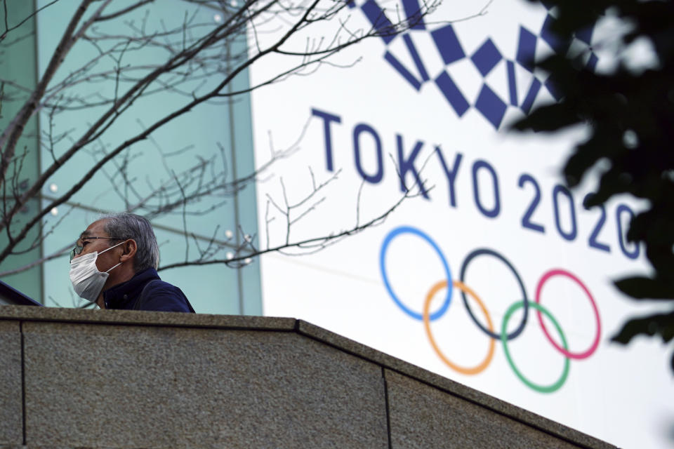 A man wearing a protective mask to help curb the spread of the coronavirus walks near the banner for the Tokyo 2020 Olympic Games Thursday, Feb. 25, 2021, in Tokyo. The Japanese capital confirmed more than 340 new coronavirus cases on Thursday. (AP Photo/Eugene Hoshiko)