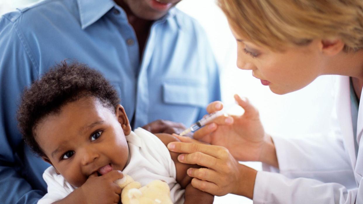 A doctor gives a 5-month-old boy an injection, while he sits in his father's lap (stock photo)