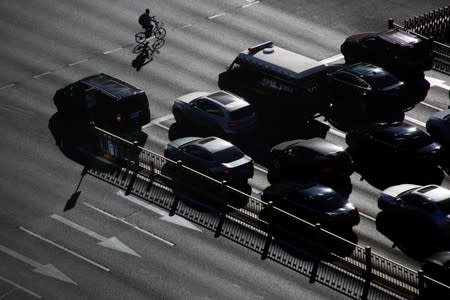 FILE PHOTO: A cyclist rides past cars that are waiting at a traffic light in central Beijing