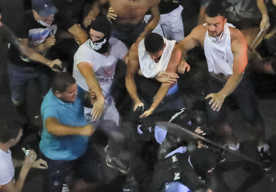 In this Friday, Aug. 10, 2018, photo, a man attempts to remove the handgun from a female riot police officer after she and a colleague fell, were left behind and ended up mobbed by people during a charge to clear the square during protests outside the government headquarters, in Bucharest, Romania. Romanian authorities say hundreds of people including two dozen riot police have received medical treatment after an anti-government protest turned violent and two weapons were stolen from riot police officers. (AP Photo/Vadim Ghirda)