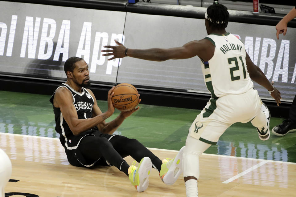 Brooklyn Nets' Kevin Durant, left, looks to pass against Milwaukee Bucks' Jrue Holiday, right, after falling to the floor during the second half of an NBA basketball game Tuesday, May 4, 2021, in Milwaukee. (AP Photo/Aaron Gash)