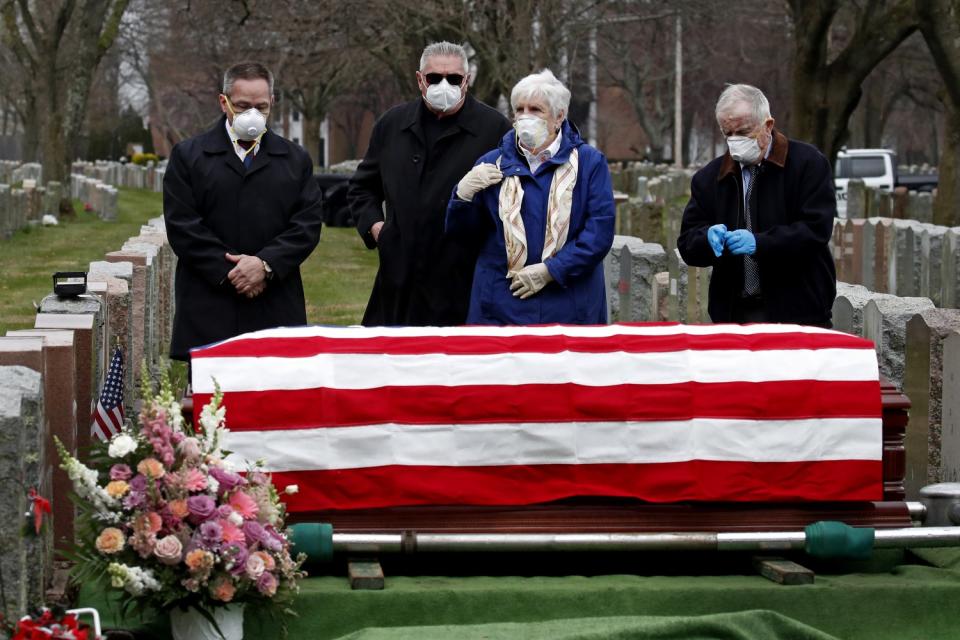 Four mourners stand next to a U.S.-flag-draped casket of a military veteran in a cemetery