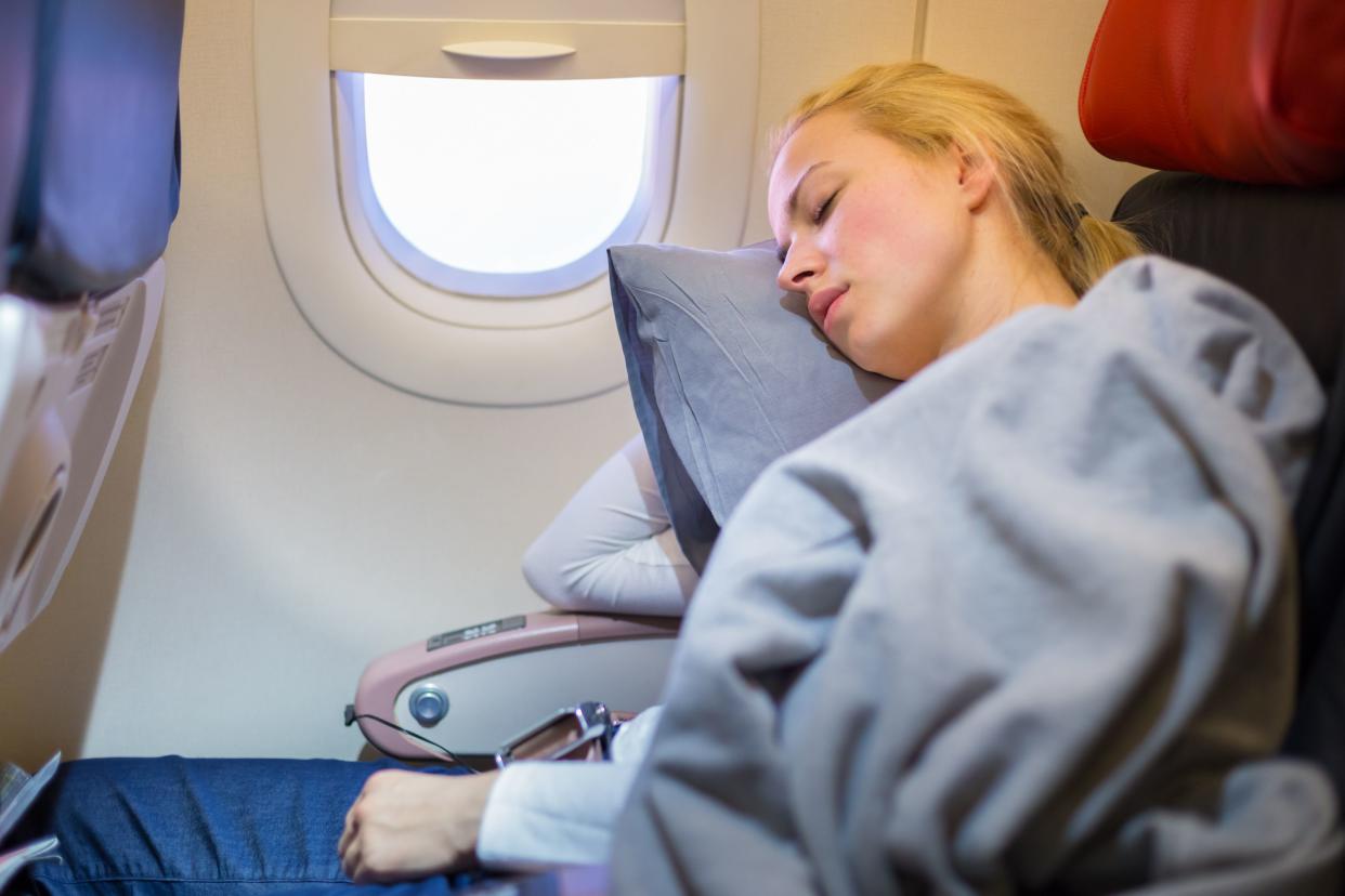 Tired blonde casual caucasian lady napping on uncomfortable seat while traveling by airplane. Commercial transportation by planes.