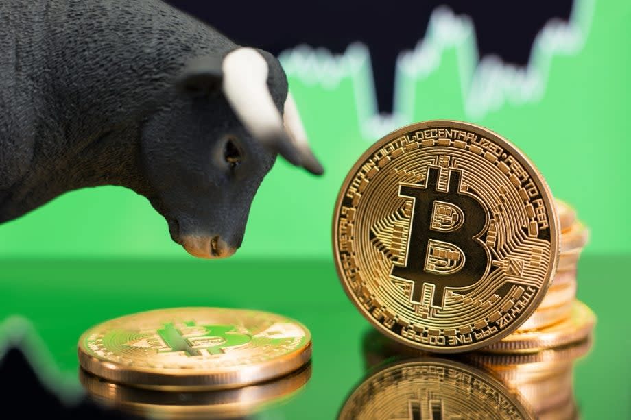 Bitcoin-Münzen und Bullen-Figur vor grünem Börsenchart