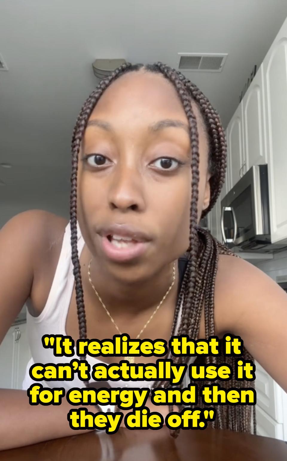 A person with braids wearing a white tank top and a necklace leans towards the camera while in a kitchen. Text on image: 