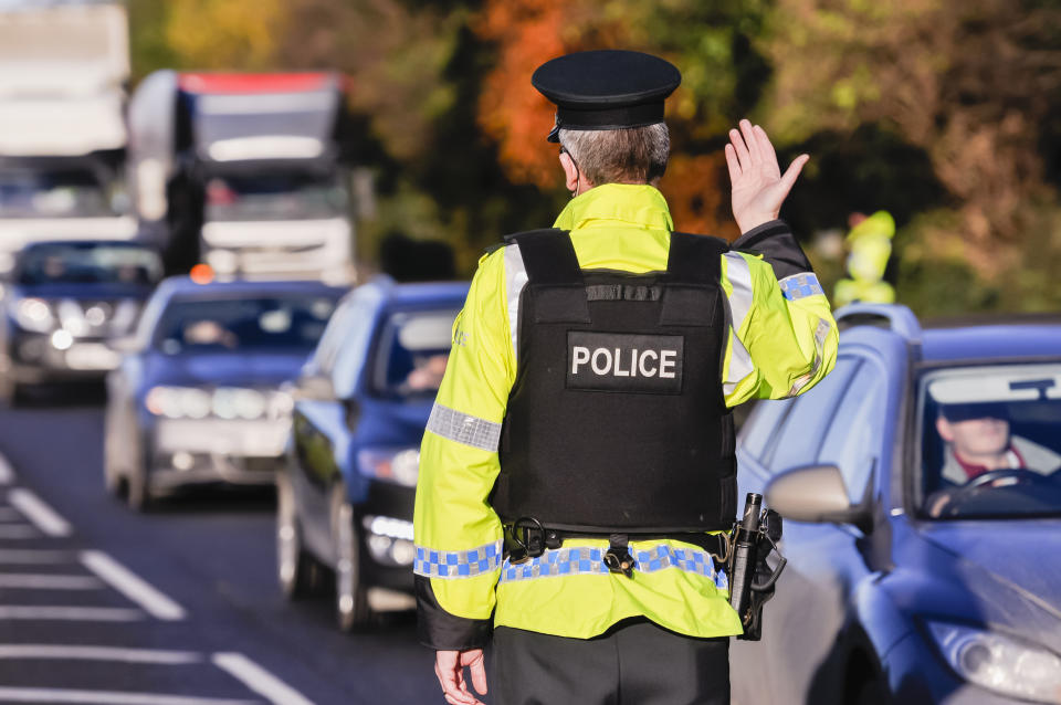 Belfast, Northern Ireland. 24 Nov 2016 - An armed PSNI officer waves on traffic during a vehicle checkpoint.