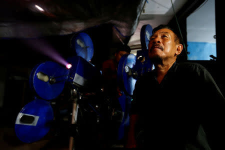 A villager sits next to a projector showing a film, during a circumcision party in Rempoa village on the outskirts of Jakarta, Indonesia, April 9, 2017. REUTERS/Beawiharta