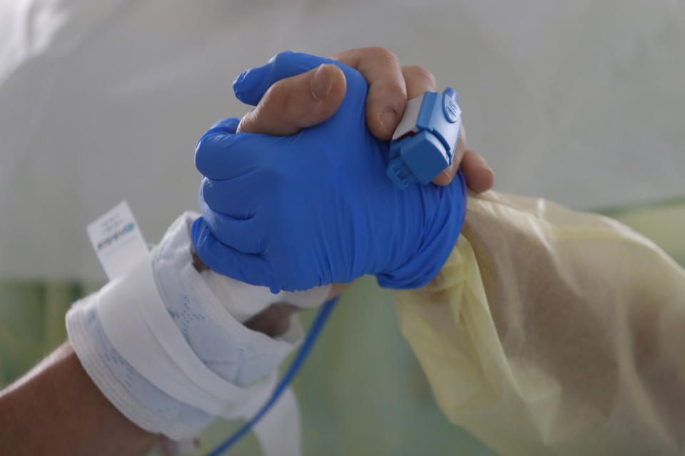 Therapist Catia Jesus holds the hand of a patient inside a COVID-19 ICU at Santa Maria hospital in Lisbon, Friday, Oct. 30, 2020. Portugal is reporting a record number of new COVID-19 cases, deaths and hospital admissions. (AP Photo/Armando Franca)