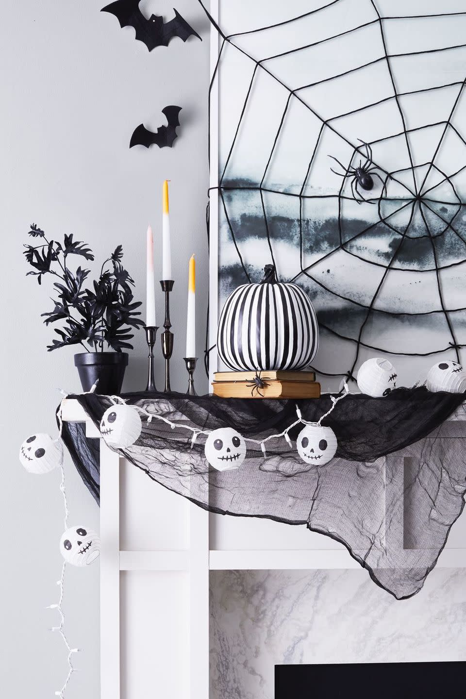 <p>Amp up a cobweb-covered mantel with a pumpkin decked out in black-and-white stripes. Pull the look together with candlesticks and string lights — with skulls, of course. </p>