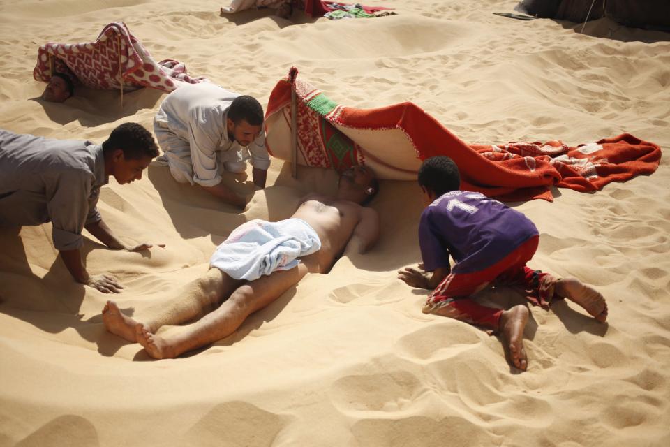 Workers help to bury a patient in the sand during his sand bath in Siwa, Egypt, August 12, 2015. (REUTERS/Asmaa Waguih)