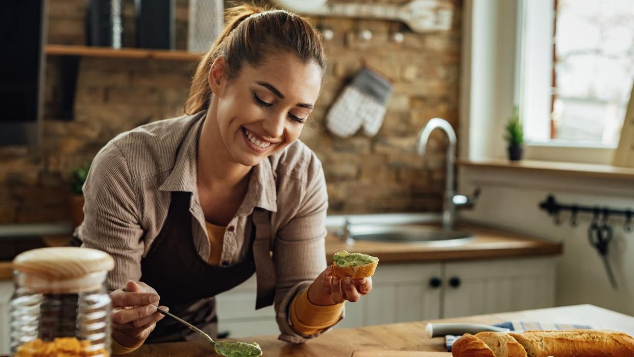 mujer sonriente preparando tostadas de aguacate en la cocina