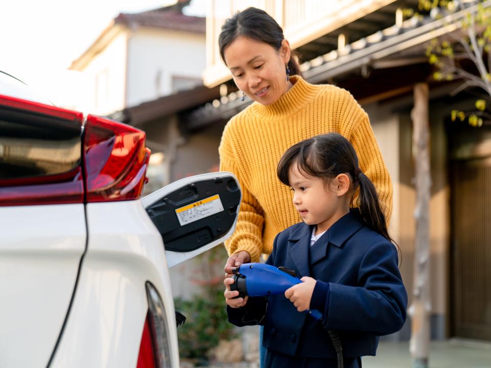 Young girl helping her mum to charge their electric car at home