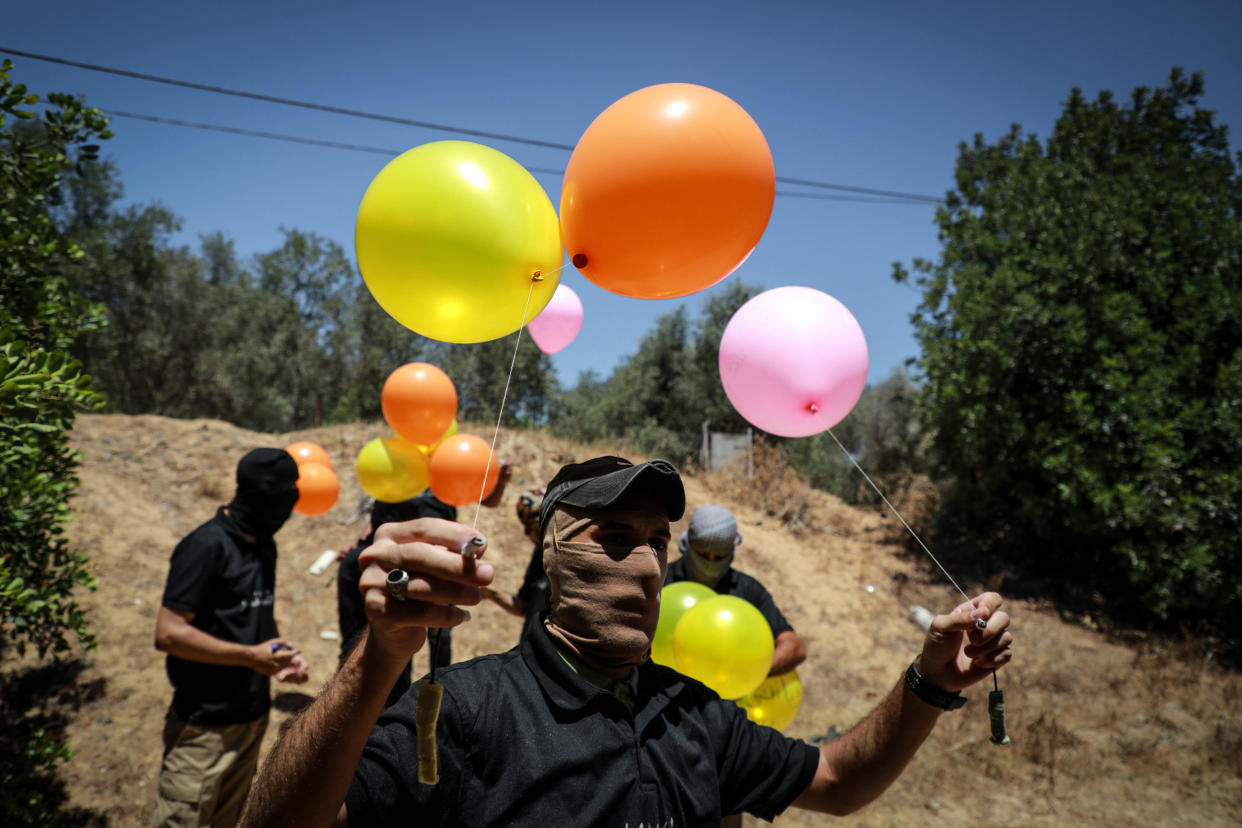 Image: Masked Palestinian supporters of the Al-Nasir Salah Al-Din Brigades prepare incendiary balloon (Majdi Fathi / NurPhoto via Getty Images)