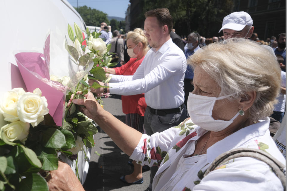 People place flowers on vans as hundreds of people turned out in Sarajevo's main street Thursday, July 9, 2020, to pay respects to eight victims of the Srebrenica massacre as three white vans carried their coffins to a final resting place. The remains of the men and boys, found in mass graves and identified through DNA analysis, will be buried in Srebrenica on Saturday, the 25th anniversary of the massacre, next to 6,610 previously found victims. (AP Photo/Kemal Softic)