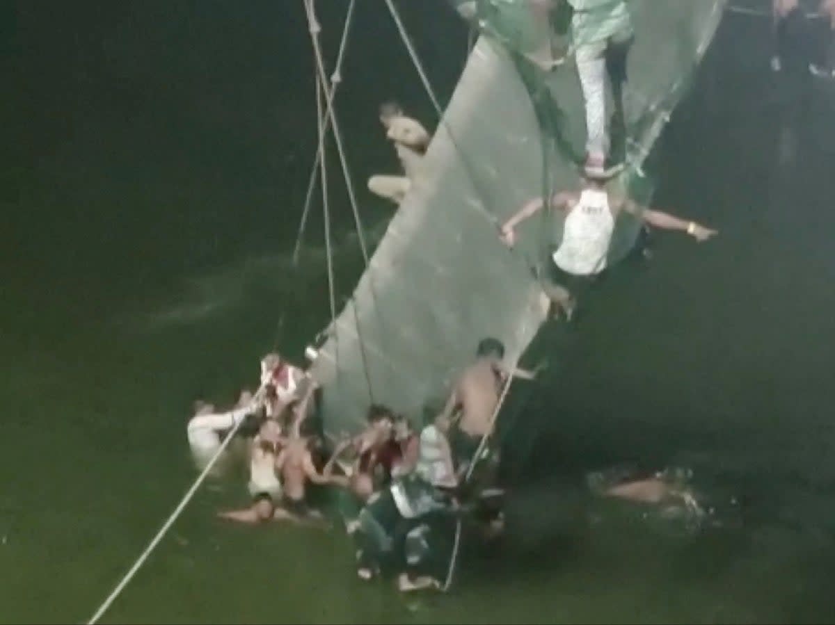 People cling on to a collapsed suspension bridge in Morbi, Gujarat (ANI/Handout via Reuters)