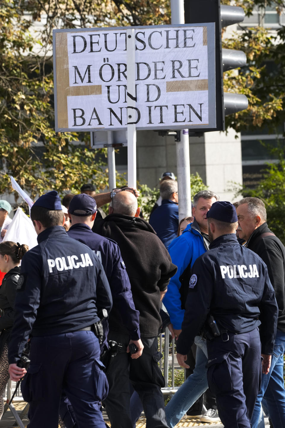 Police officers leads way a man with a poster reading 'German killers and bandits' alongside a march to support the opposition against the governing populist Law and Justice party in Warsaw, Poland, Sunday, Oct. 1, 2023. Polish opposition leader Donald Tusk seeks to boost his election chances for the parliament elections on Oct. 15, 2023, leading the rally in the Polish capital. (AP Photo/Czarek Sokolowski)