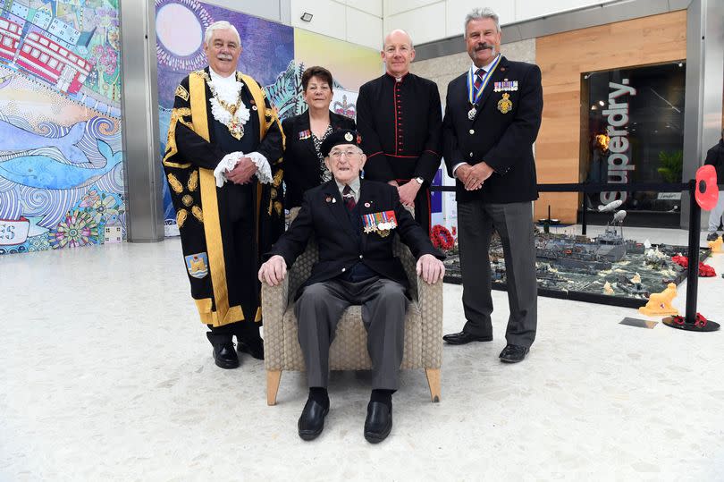 Richard Pelzer sits on a chair in the Quadrant shopping centre.
Behind him: (from L to R) Lord Mayor of Swansea Paxton Hood-William wearing his mayoral robes, Armed Forces Champion for the City and County of Swansea Wendy Lewis, the Reverend Canon of St Mary's Church (which held a special D Day service where Cpl Pelsar was the special guest) Justin Davies, and Phil Flowers MBE who has played a pivotal role in supporting local veterans for the last four decades