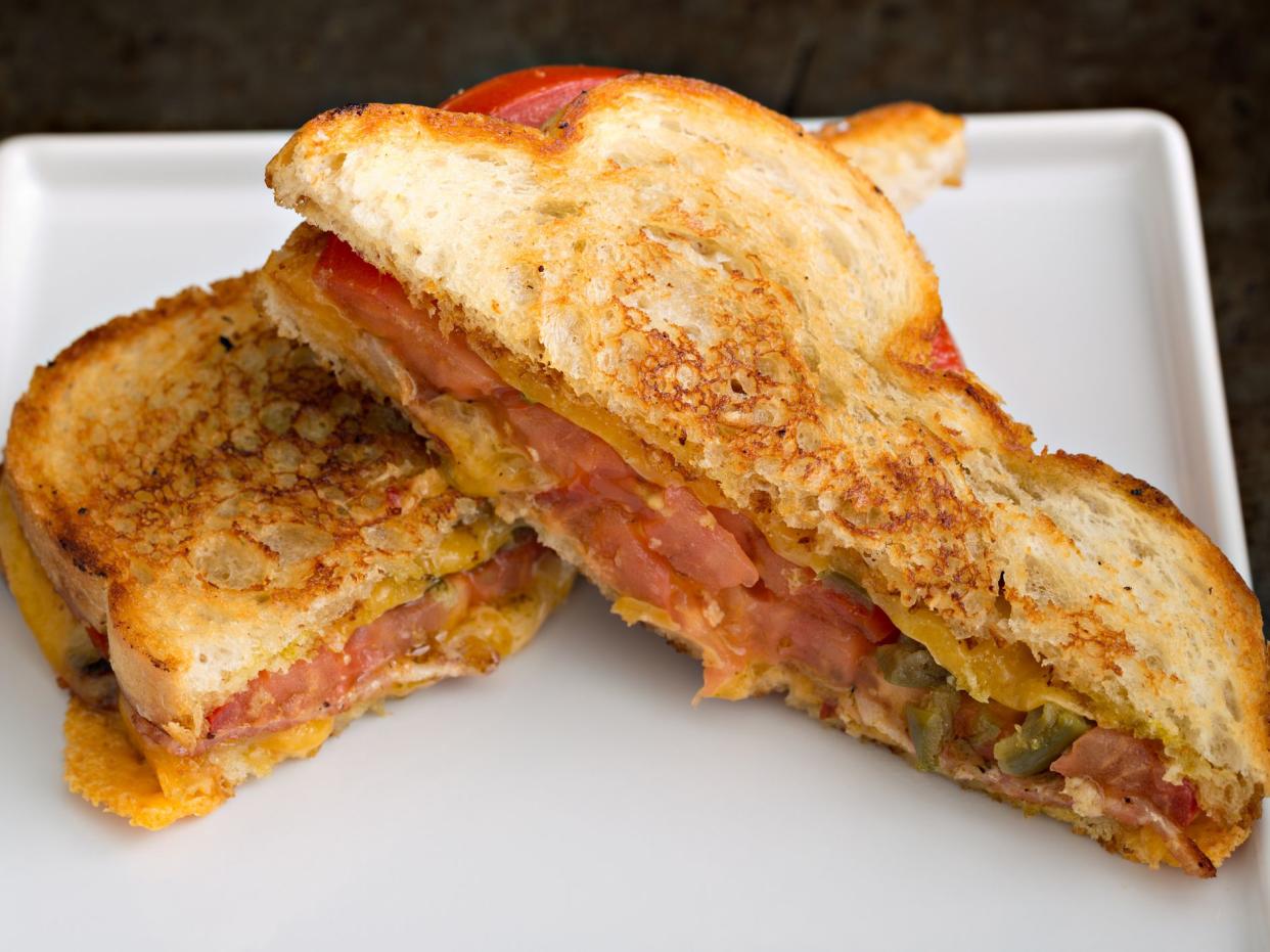 "A high angle close up shot of a grilled cheese, bacon and tomato sandwich on a white plate."