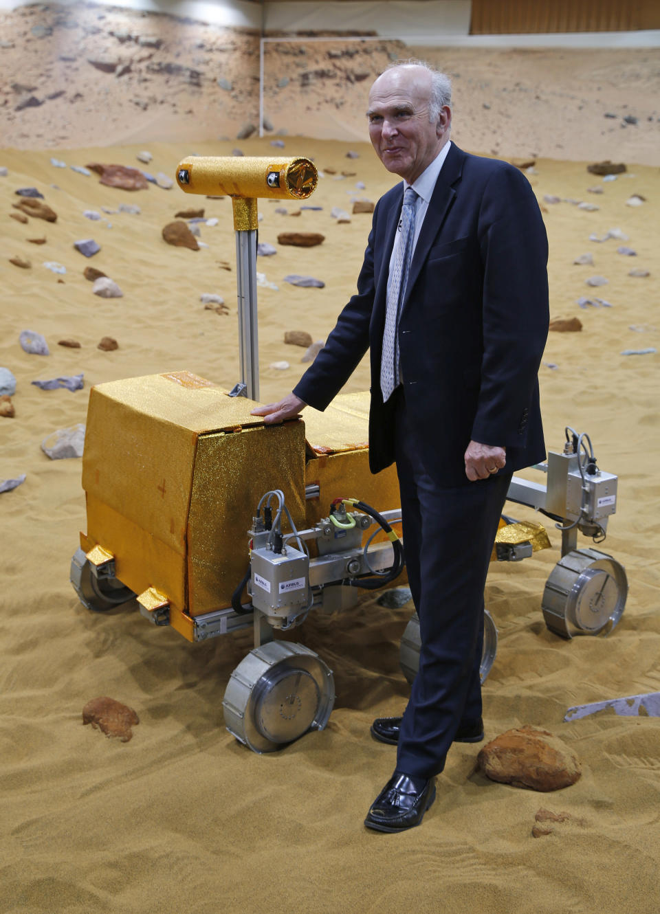 Britain's Business Secretary Vince Cable poses for the photographers next to a robotic vehicle being tested on the 'Mars Yard Test Area', the testing ground of the European Space Agency’s ExoMars program scheduled for 2018, in Stevenage, England, Thursday, March 27, 2014. It looks like a giant sandbox - except the sand has a reddish tint and the “toys” on display are very expensive prototypes designed to withstand the rigors of landing on Mars. The scientists here work on the development of the autonomous navigation capabilities of the vehicle, so by being in communication with controllers on earth twice a day, will be able to use the transmitted information to navigate to new destinations on Mars. (AP Photo/Lefteris Pitarakis)