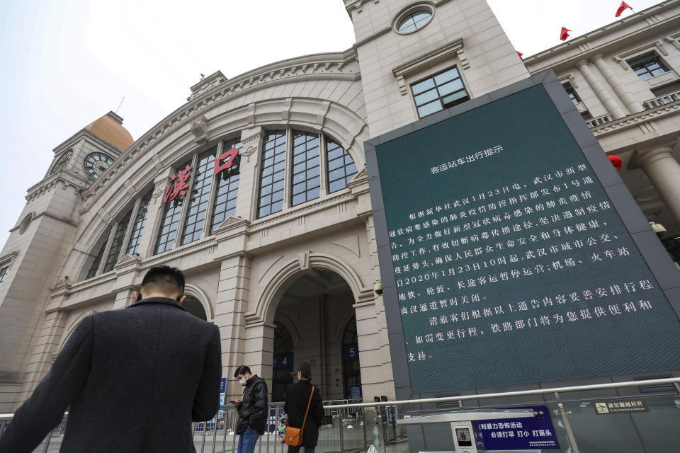 People walk past a billboard announcing the closure of the Hankou Railway Station in Wuhan in central China's Hubei Province, Thursday, Jan. 23, 2020. China closed off a city of more than 11 million people Thursday in an unprecedented effort to try to contain a deadly new viral illness that has sickened hundreds and spread to other cities and countries amid the Lunar New Year travel rush. (Chinatopix via AP)