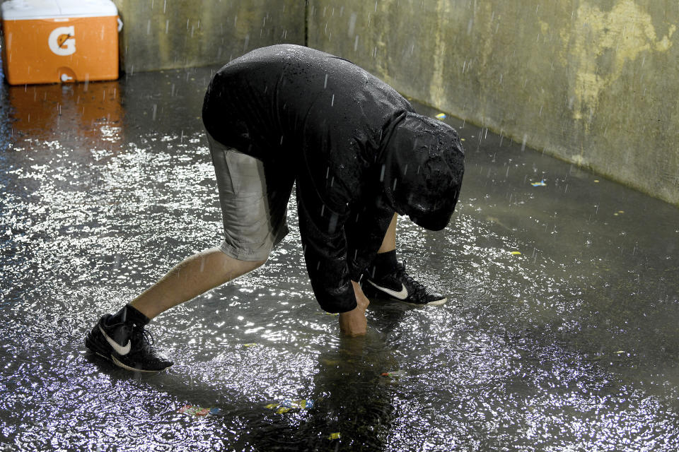 A member of the Detroit Tigers grounds crew works to clear the drain in the Milwaukee Brewers dugout during a weather delay at a baseball game in Detroit, Tuesday, Sept. 14, 2021. (AP Photo/Lon Horwedel)