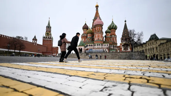 A couple walk in front of the Kremlin&#39;s Spasskaya Tower and St. Basil&#39;s Cathedral in downtown Moscow. 