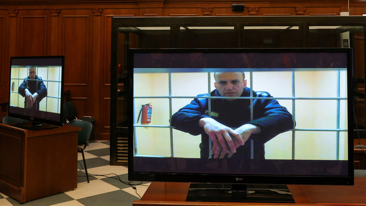 Alexei Navalny, shown behind bars, is seen on screens positioned on tables in a courtroom.