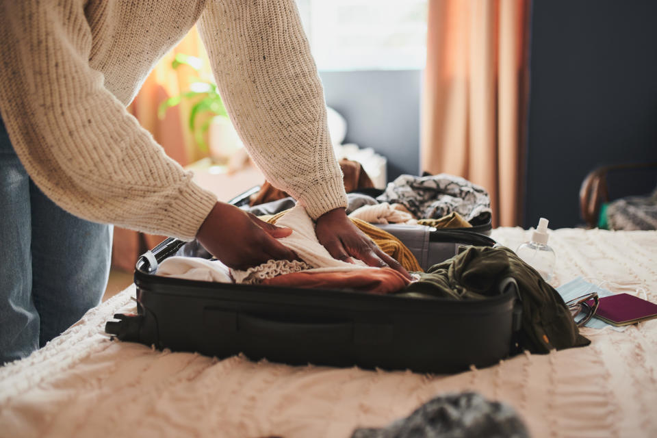 A person packing a suitcase on a bed in a cozy room. Various clothing items and a passport are visible