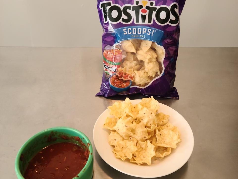 Bag of Tostitos scoops next to plate of chips and bowl of salsa.