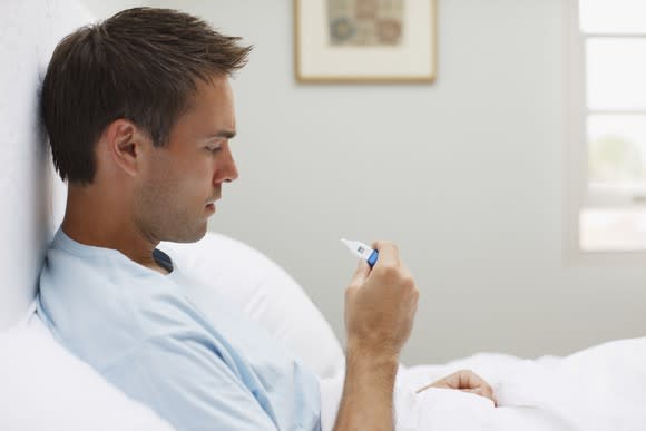 A man in bed looking at a thermometer