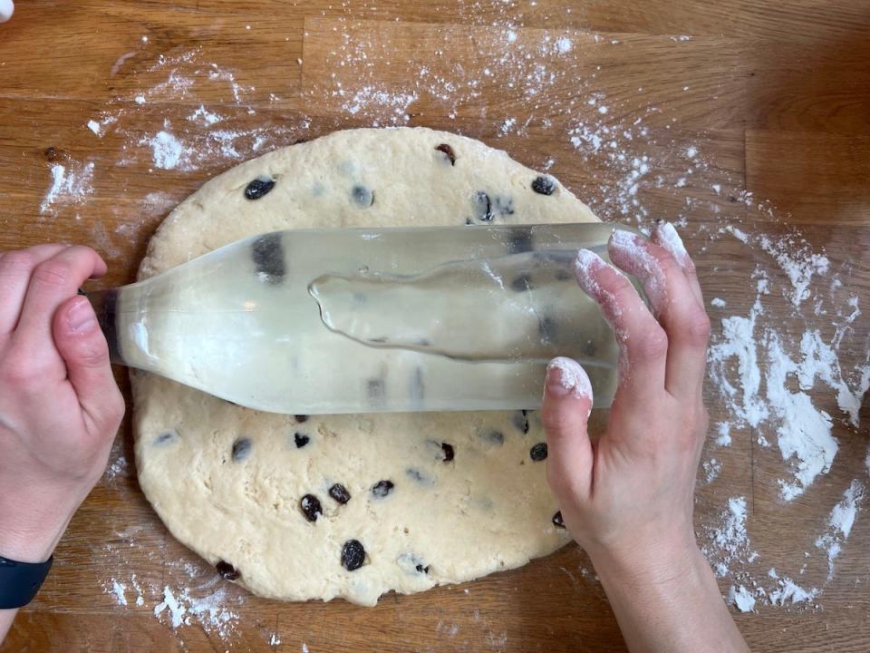 An overhead shot shows a woman's hands rolling scone dough with a glass bottle of water.