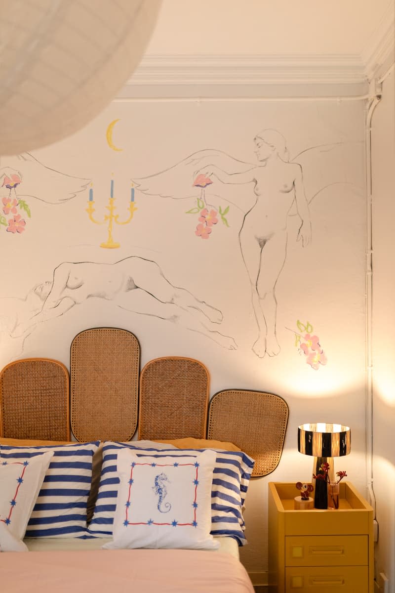 Artwork on wall behind bed with cane headboard in neutral bedroom.