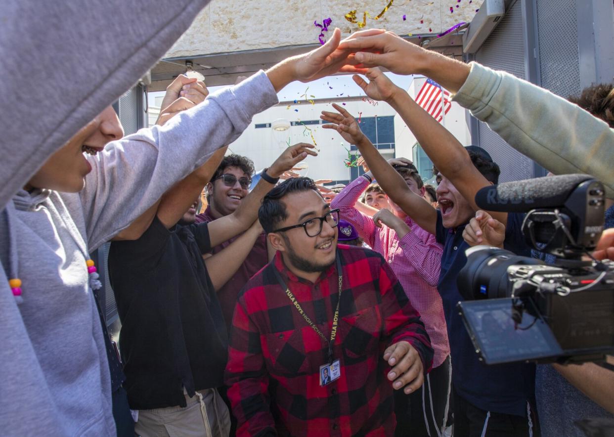 A teacher walks between two lines of cheering students holding up their arms