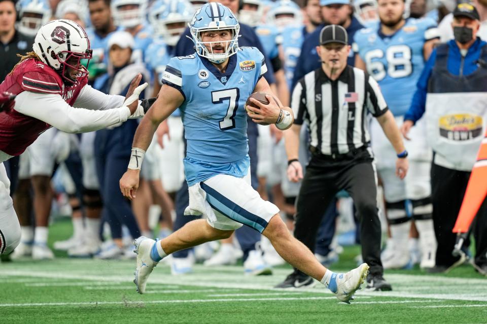 North Carolina quarterback Sam Howell picks up yards on the run as South Carolina defensive lineman Zacch Pickens, left, gives chase Thursday in the Duke’s Mayo Bowl.