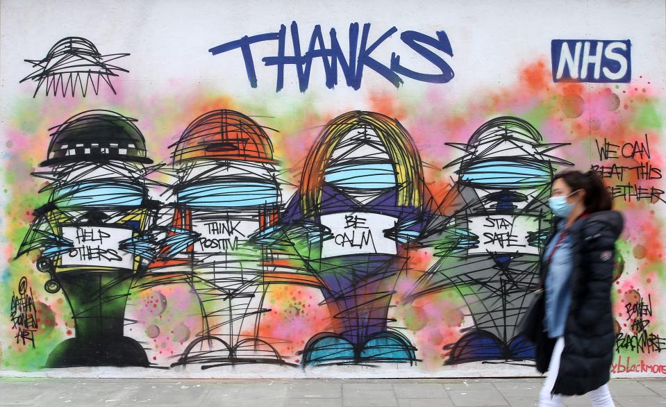 A pedestrian wearing PPE (personal protective equipment), including a face mask as a precautionary measure against COVID-19, walks past street art graffiti praising the workers od Britain's NHS (National Health Service) and other key workers, by artists Nathan Bowen and Harry Blackmore, in London on April 23, 2020. on May 13, 2020, as people start to return to work after COVID-19 lockdown restrictions were eased. - Britain's economy shrank two percent in the first three months of the year, rocked by the fallout from the coronavirus pandemic, official data showed Wednesday, with analysts predicting even worse to come. Prime Minister Boris Johnson began this week to relax some of lockdown measures in order to help the economy, despite the rising death toll, but he has also stressed that great caution is needed. (Photo by ISABEL INFANTES / AFP) / RESTRICTED TO EDITORIAL USE - MANDATORY MENTION OF THE ARTIST UPON PUBLICATION - TO ILLUSTRATE THE EVENT AS SPECIFIED IN THE CAPTION (Photo by ISABEL INFANTES/AFP via Getty Images)