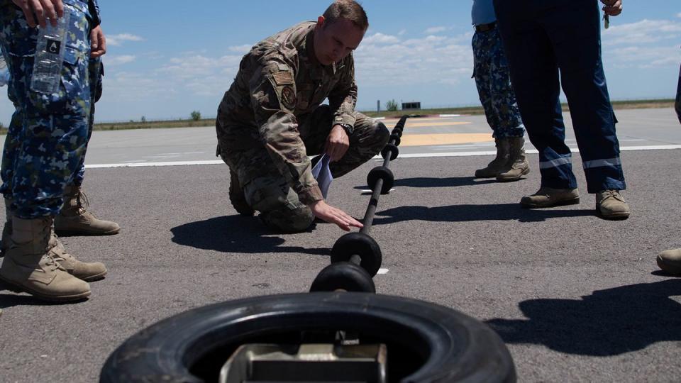 U.S. Air Force Staff Sgt. Devon Schafer, 435th Contingency Response Support Squadron air advisor, demonstrates how to find flaws in the Barrier Arresting Kit cable to members of the Romanian air force at Fetesti Air Base, Romania, July 19. (Airman 1st Class Alexcia Givens/Air Force)

