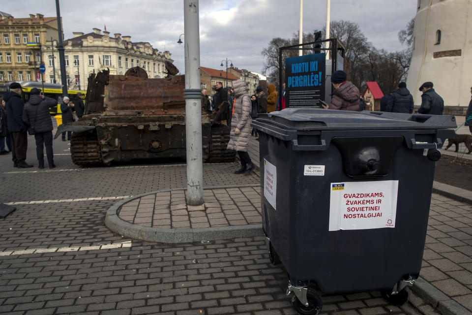 A garbage container displays a sign with writing reading "For carnations, candles and Soviet nostalgia", to be used for flowers laid by ethnic Russians on the destroyed Russian tank T-72B, installed as a symbol of war marking the first anniversary of Russia's full-scale invasion of Ukraine, at Cathedral Square in Vilnius, Lithuania, Wednesday, March 1, 2023. Some ethnic Russians in the Baltic states have placed flowers at displays of burnt-out Russian tanks seized by Ukrainians, making a gesture of homage and support for Russia's war against Ukraine. (AP Photo/Mindaugas Kulbis)