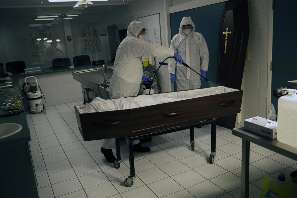 Workers, wearing a full protective equipment, disinfect the casket of someone who has died of coronavirus at the Fontaine funeral home during a partial lockdown to prevent the spread of coronavirus in Charleroi, Belgium, Wednesday, April 15, 2020. (AP Photo/Francisco Seco)