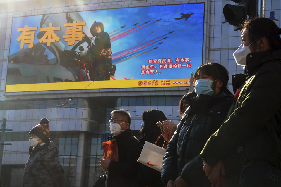 Residents wearing face masks wait to cross a traffic intersection near a large screen promoting the Chinese People's Liberation Army Airforce, in Beijing, Monday, Jan. 9, 2023. The Chinese military held large-scale joint combat strike drills starting Sunday, sending war planes and navy vessels toward Taiwan, both the Chinese and Taiwanese defense ministries said. (AP Photo/Andy Wong)