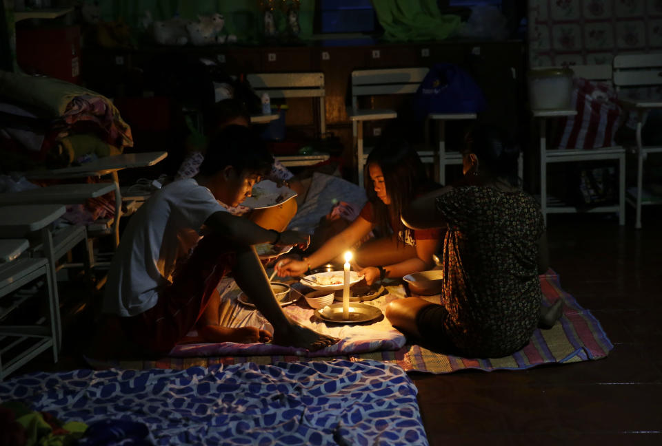 FILE- In this Saturday, Sept. 15, 2018, photo, a family shares a meal using a flashlight inside a temporary evacuation center as electricity was shut-off following the onslaught of Typhoon Mangkhut in Tuguegarao City in Cagayan province, northeastern Philippines. (AP Photo/Aaron Favila, File)