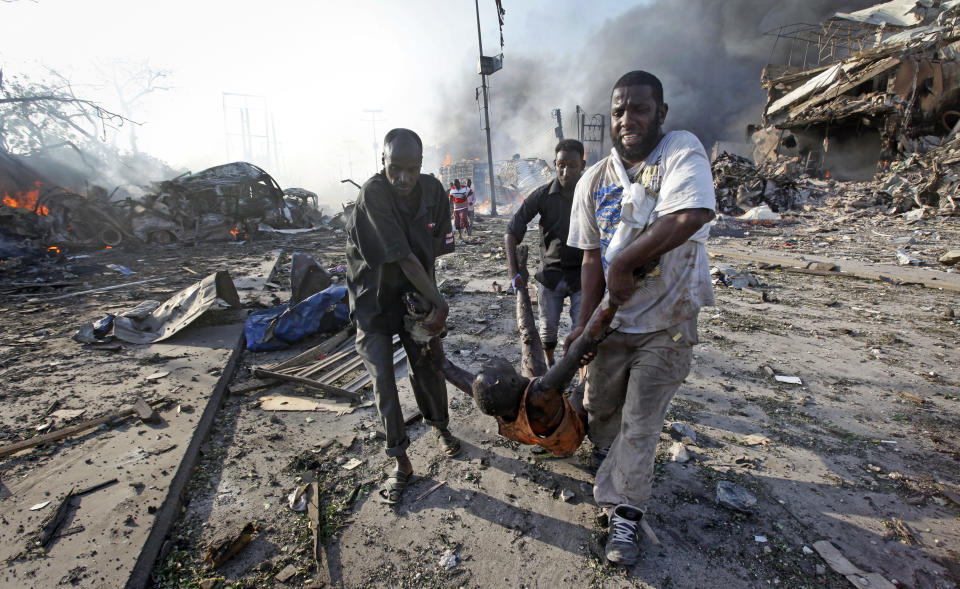 FILE - In this Saturday, Oct. 14, 2017 file photo, Somalis remove the body of a man killed in a huge explosion from a truck bomb that killed at least 20 people, in the capital Mogadishu, Somalia. U.N. experts said in a report circulated Tuesday, Nov. 12, 2019 that al-Shabab extremists in Somalia remain "a potent threat" to regional peace and are manufacturing home-made explosives, expanding their revenue sources and infiltrating government institutions. (AP Photo/Farah Abdi Warsameh, File)