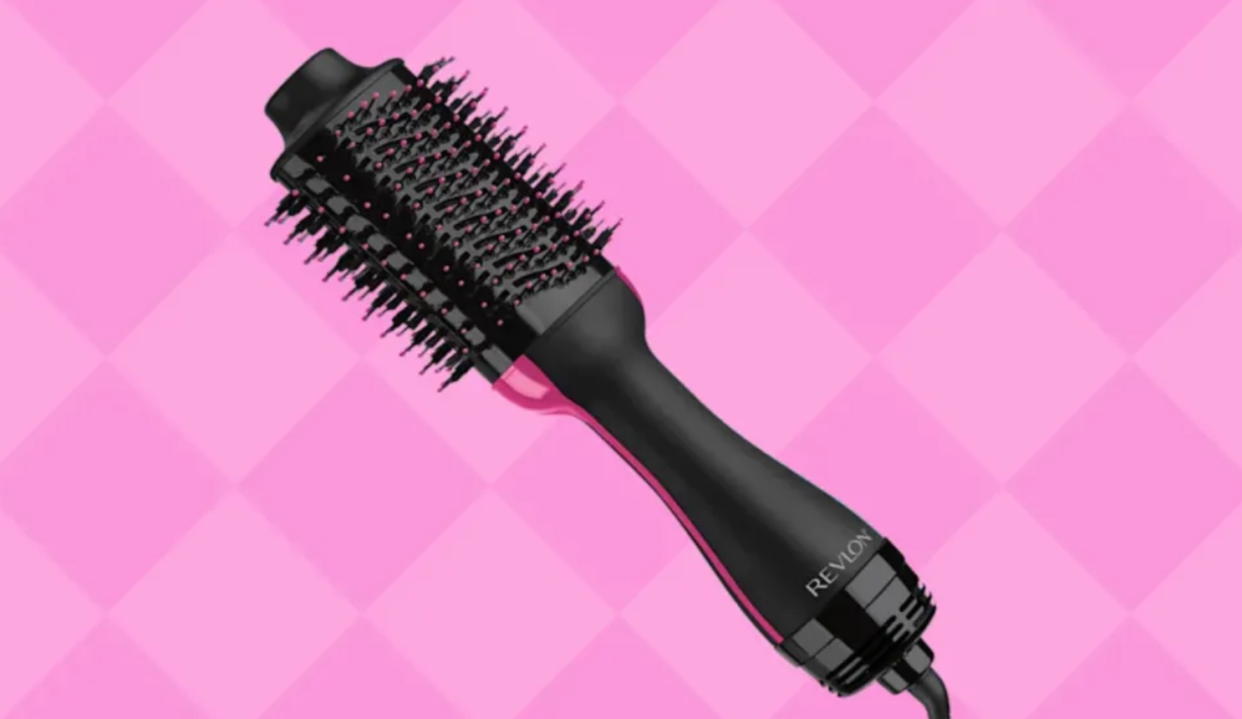 A black and pink Revlon brand blow drying brush is set against a bright pink background. 