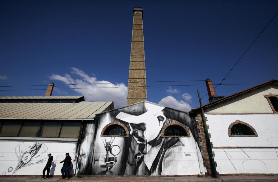 In this photo taken on Wednesday March 12, 2014, pedestrians walk past work by Greek street artist iNO, at an exhibition space created out of an old gasworks on central Pireos Street in Athens. Greece has attracted international street artists to its capital, due to the availability of commissioned work and relatively lax anti-graffiti law. (AP Photo/Dimitri Messinis)