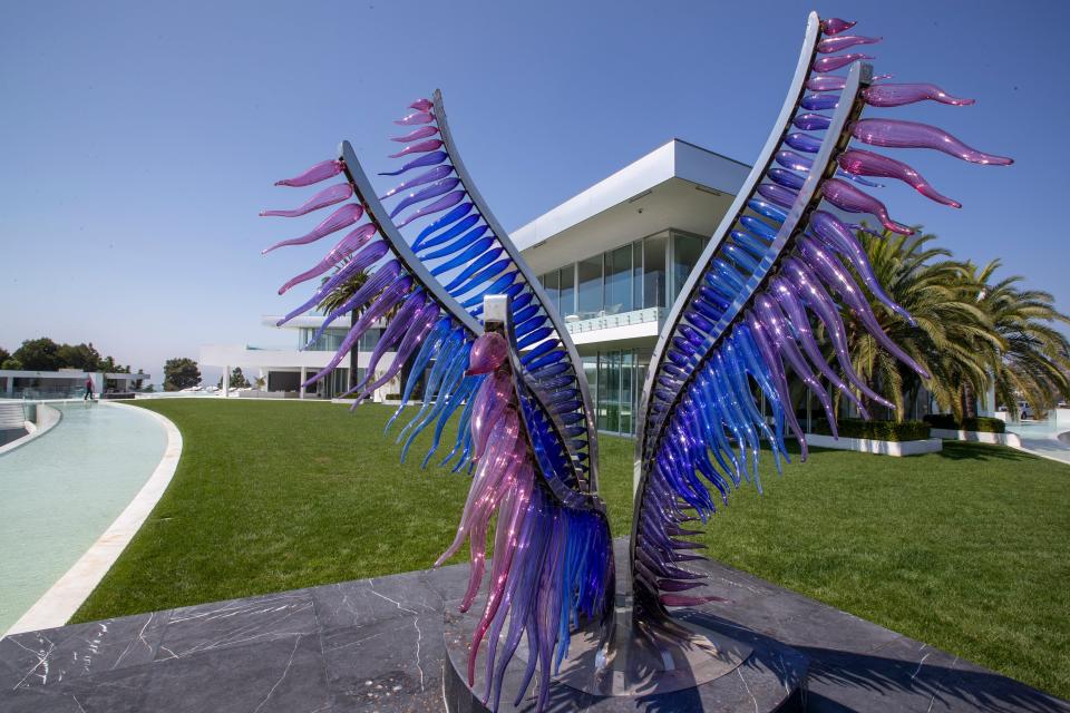 a blue and purple sculpture of wings in front of green grass and a white building at mansion The One Bel Air