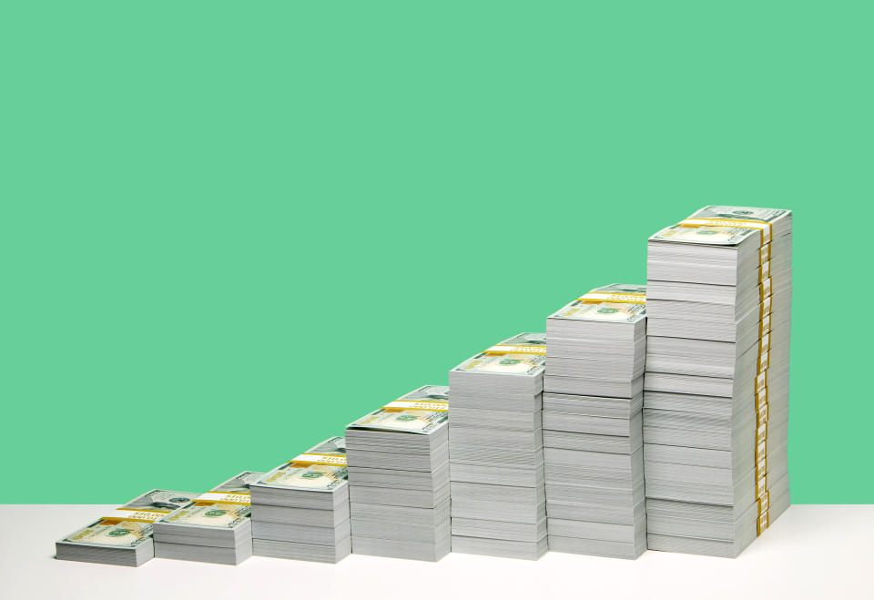 Stacks on US $100 bill bundles in ascending order on white shelf, green background. A Birkin bag can cost upwards of tens of thousands of dollars. (Getty)