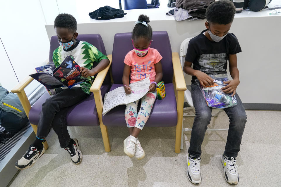 FILE - Siblings Amechi, 7, left, Chizara, 5, center and Kenechi Acholonu, 9, enjoy gifts from the hospital as they wait in the observation area after being inoculated with the first dose of the Pfizer COVID-19 vaccine for children 5 to 11 years at The Children's Hospital at Montefiore, Wednesday, Nov. 3, 2021, in the Bronx borough of New York. First shots are averaging about 300,000 per day. (AP Photo/Mary Altaffer, File)