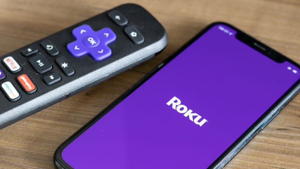  Roku remote next to iPhone with Roku logo on its screen. 