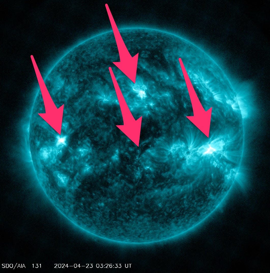 blue telescope view of the sun in space with pink arrows pointing to three bright spots and one darker spot with wavy lines